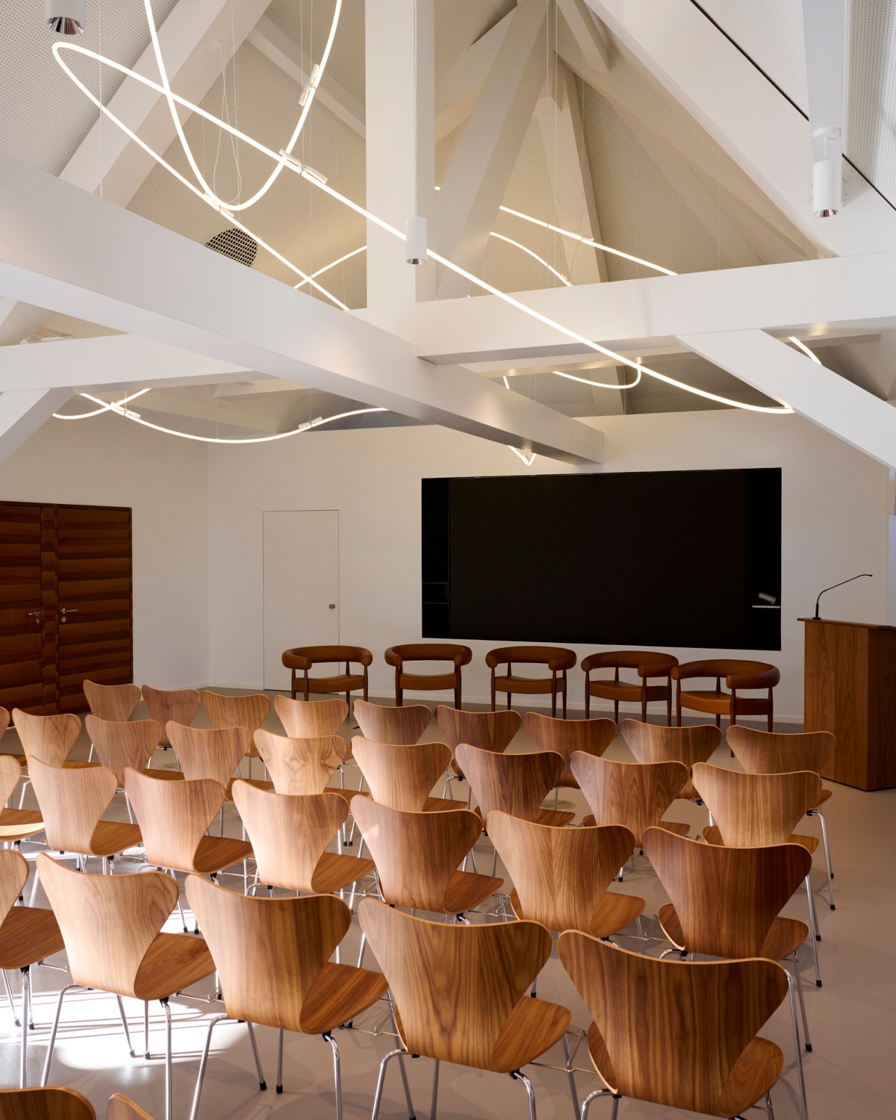 Wooden chairs with curved backs arranged in rows in a modern conference room with white ceiling beams