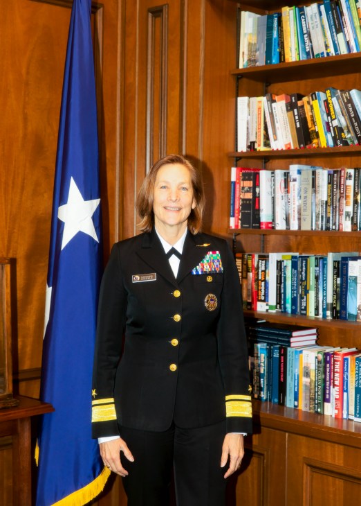 Rear admiral Shoshana Chatfield in naval uniform standing in office with bookshelf and flag