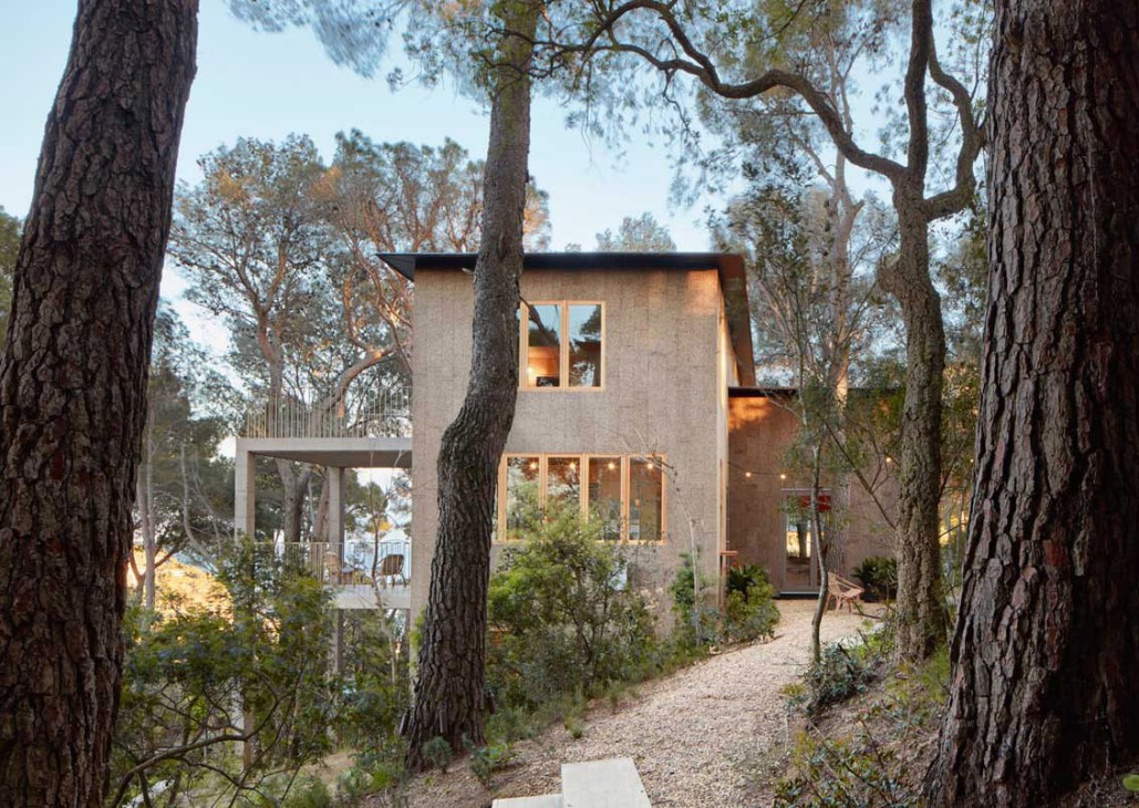 Modern timber house nestled among tall trees with large windows and a metal-railed upper deck.