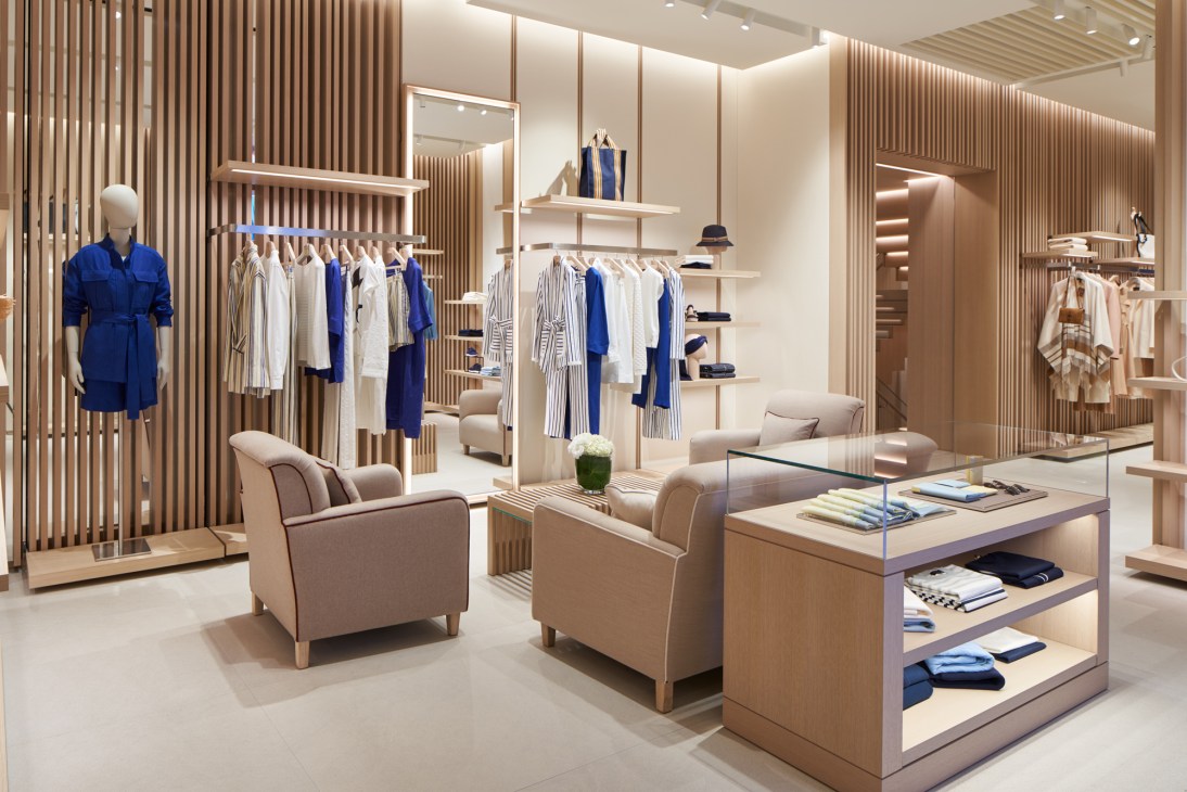 Modern retail interior with wood slat walls, beige seating area, clothing displays and glass display table