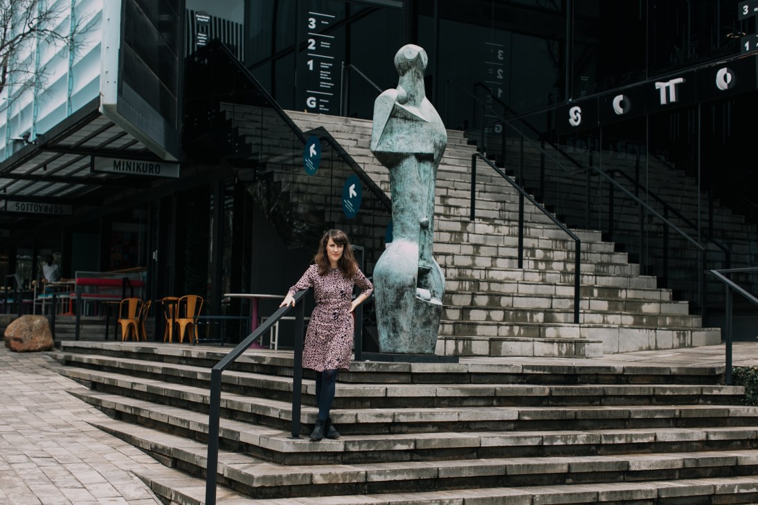 Lucy MacGarry standing on stone steps next to a large bronze sculpture