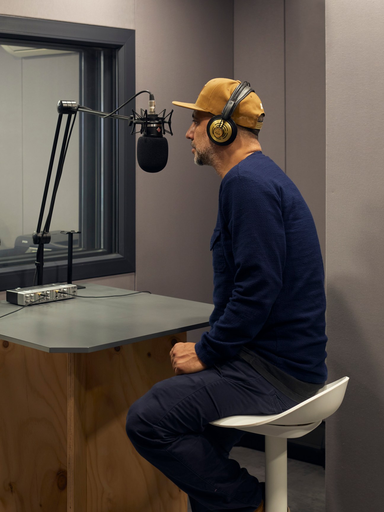 Man in yellow cap and blue sweater recording at microphone in podcast studio with headphones