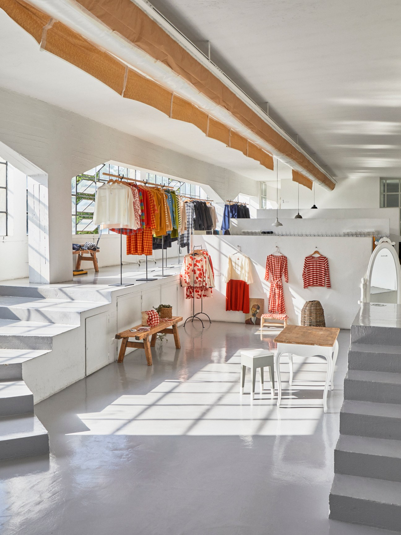 Bright studio space with clothing displayed on racks and wooden beams overhead.