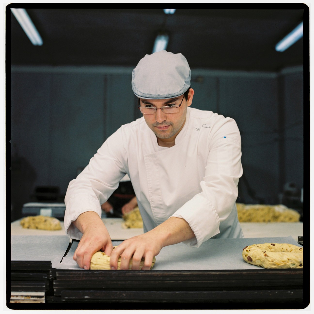 Chef in white uniform and cap carefully slicing traditional German Lebkuchen gingerbread in professional bakery kitchen
