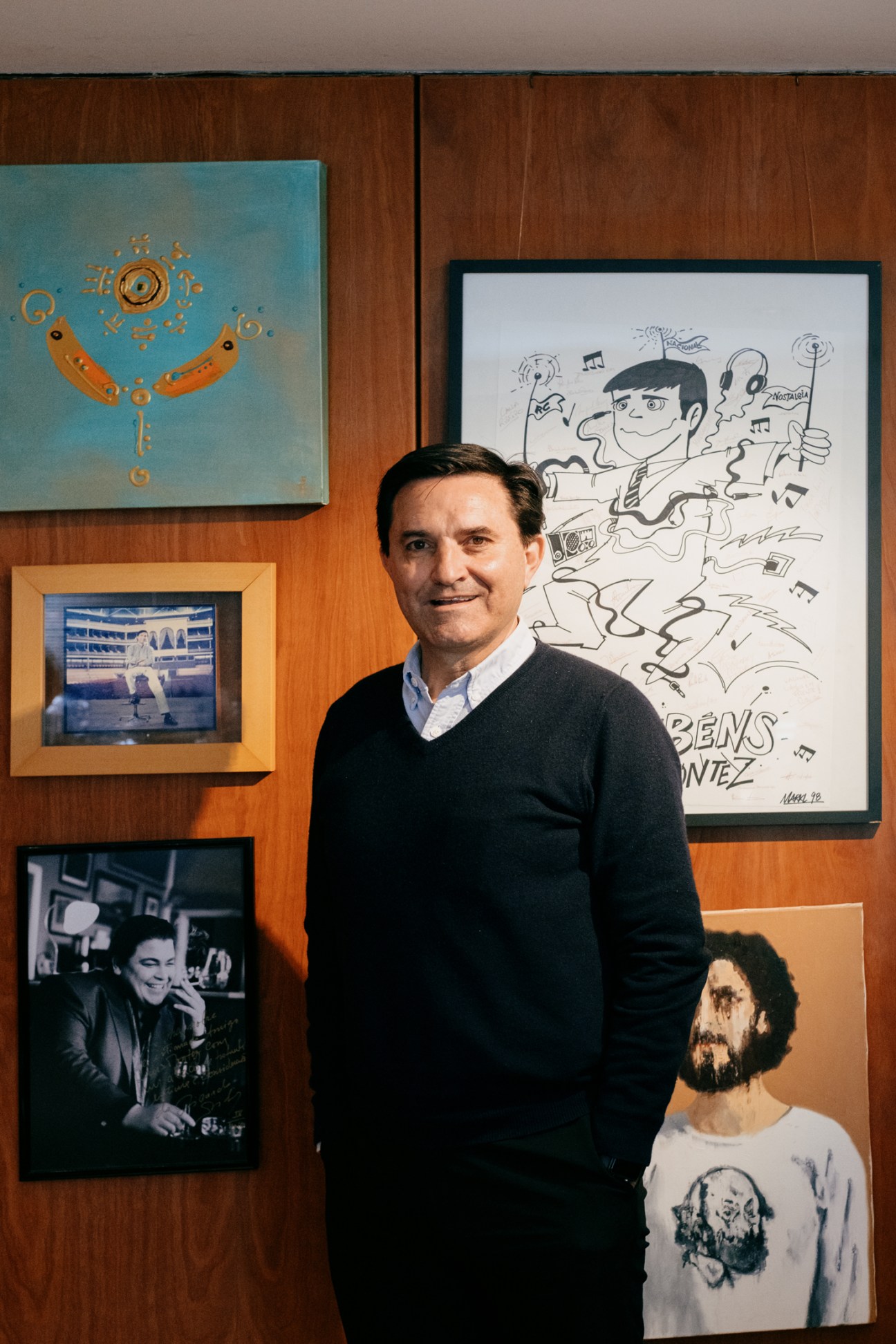 Luis Montez stands in his office surrounded by framed artwork and music memorabilia on wooden walls
