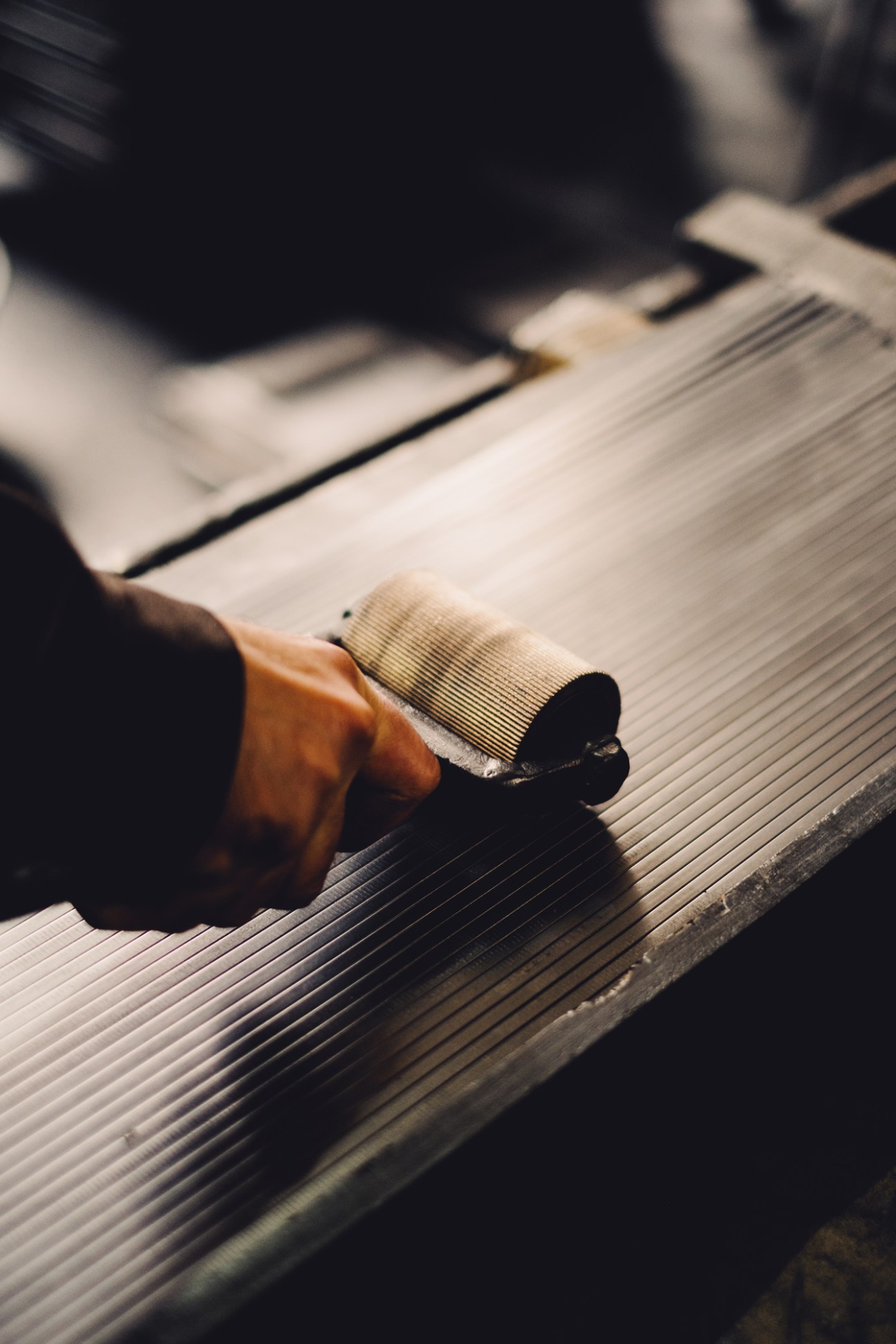 Close-up of a hand using a plane tool to smooth ridged wooden pencil slats in a workshop