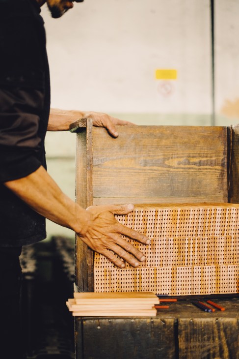Hands positioning wooden slats with woven cane material on a workbench during pencil manufacturing