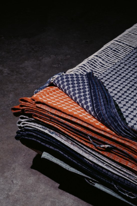 Stack of folded textiles with geometric patterns in orange, blue and white colors on dark surface
