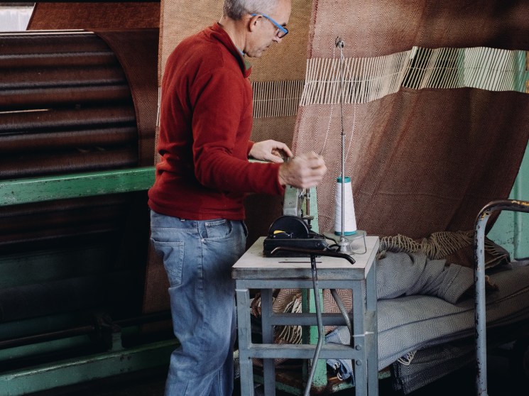 Man in red sweater operating wool processing machinery at A Transformadora textile factory in Covilhã, Portugal