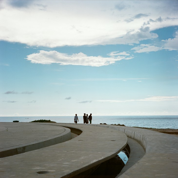 Concrete curved walkway or promenade extending toward the ocean with people visible in the distance