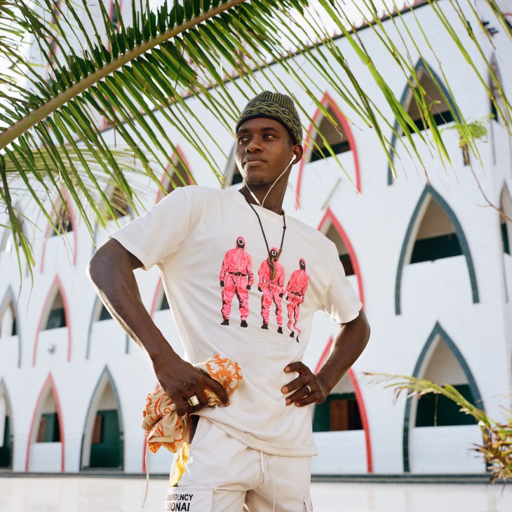 Young man in white t-shirt and beanie with earbuds under palm fronds