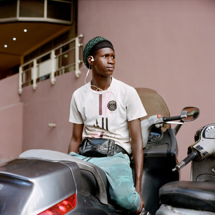Young person in Paris Saint-Germain jersey with headphones sitting between motorcycles on street