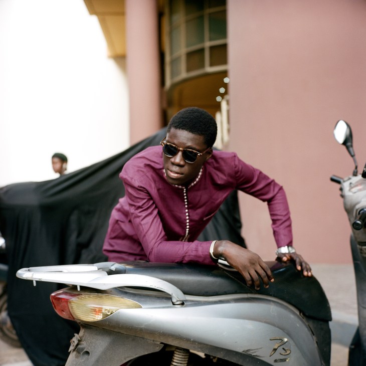 Young man in burgundy shirt and sunglasses sitting on a motorcycle