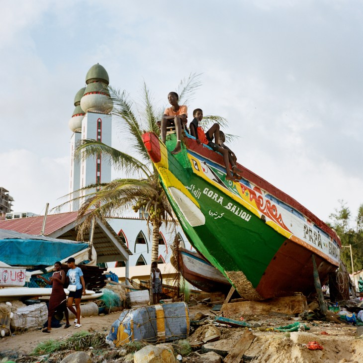 Colorful fishing boat beached on shore near white mosque with green domes and palm trees in Dakar