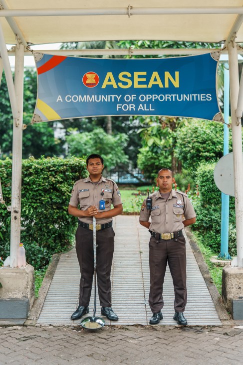 Two security guards in uniform standing under an ASEAN banner on a wooden walkway