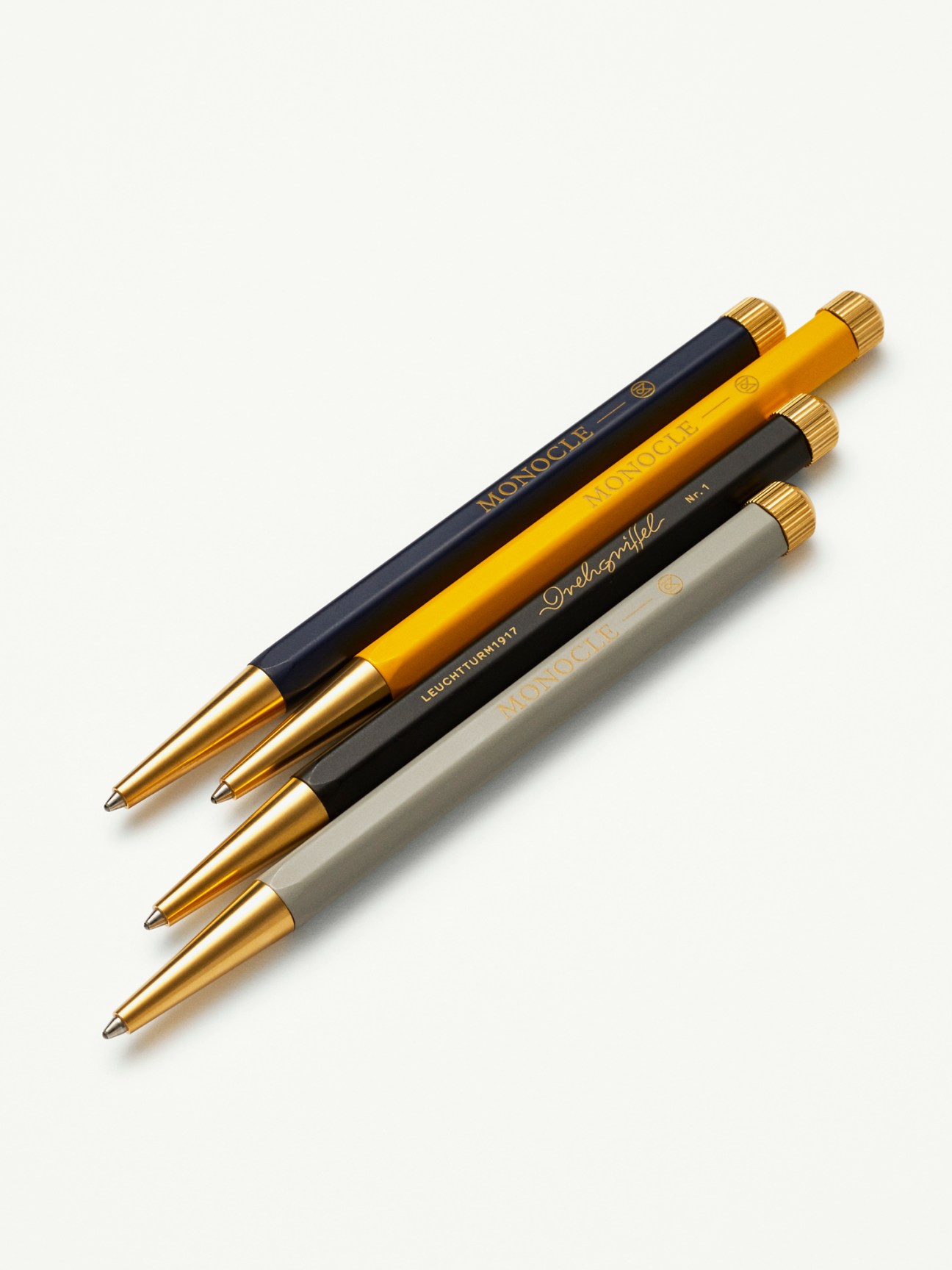 Four drehgriffel pens by Leuchtturm1917 x Monocle in black, yellow, dark and light grey with gold accents.