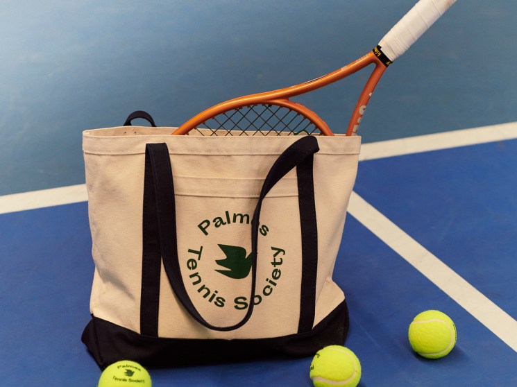 Palmes Tennis Society canvas tote bag with tennis racket and yellow tennis balls on blue court surface