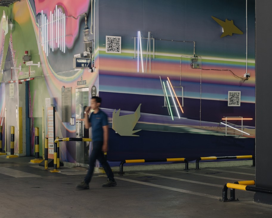 Person walking past large colorful mural in industrial warehouse space with barriers and equipment visible