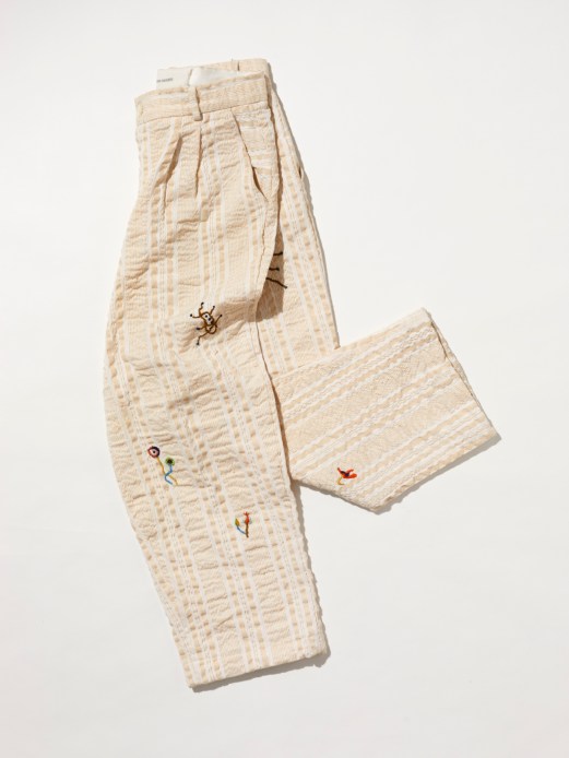 Cream colored textured pants with small colorful embroidered details scattered across the fabric