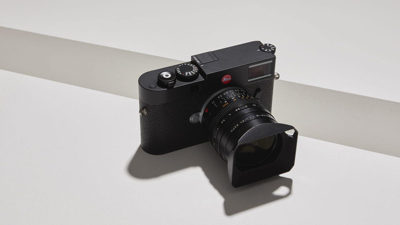 Black Leica M rangefinder camera with lens and hood on white surface
