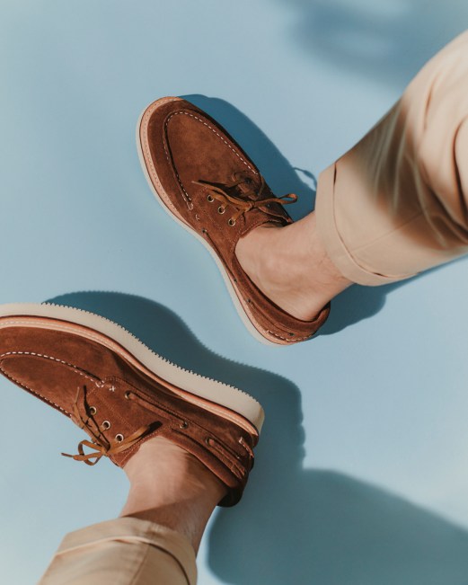 Person wearing brown leather boat shoes and beige trousers against cloudy sky background