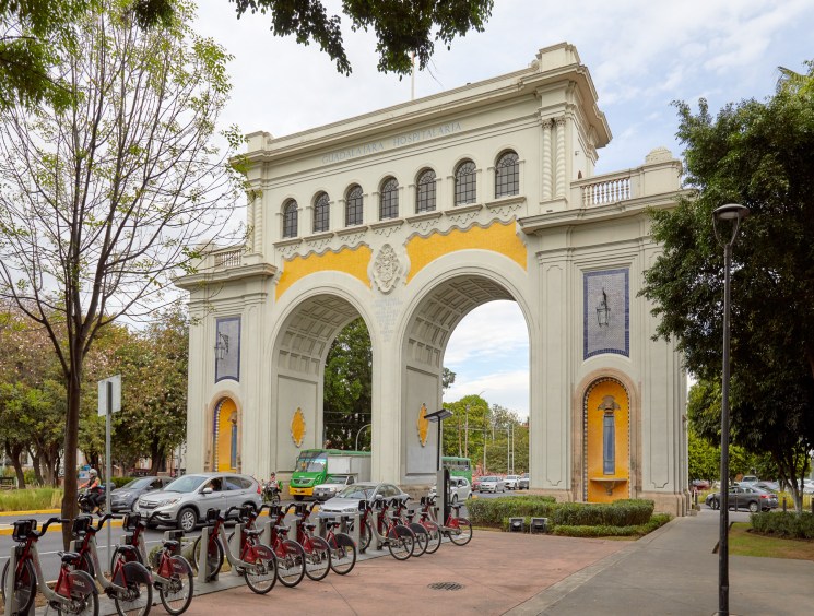 Grand neoclassical arch monument on a busy tree-lined street.
