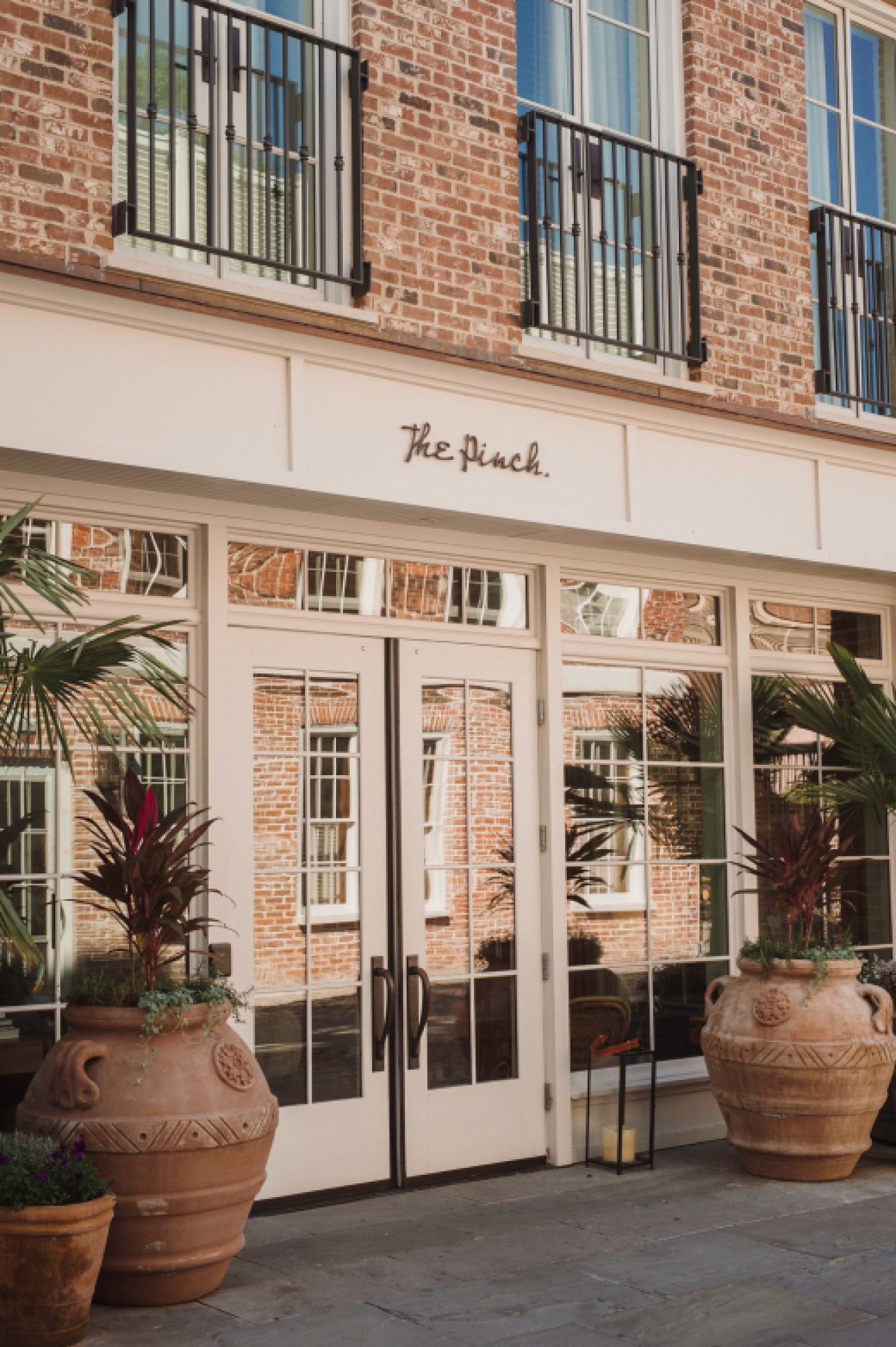 The Pinch hotel entrance with white storefront, glass doors, and decorative planters on brick paved street