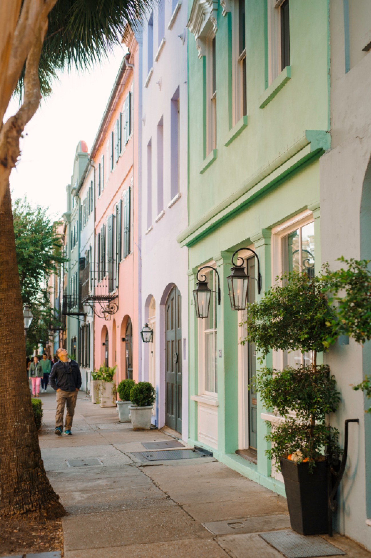 Pastel-colored historic buildings line a tree-shaded sidewalk in Charleston's downtown district