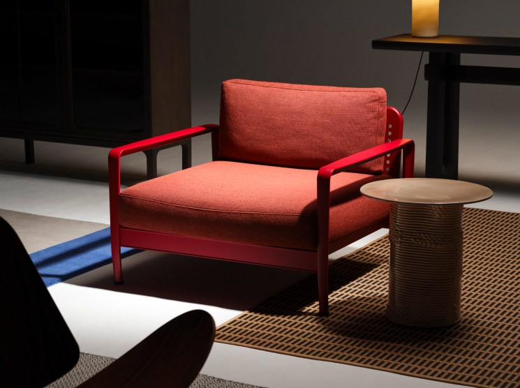 Red upholstered armchair with matching frame alongside round side table and table lamp in modern interior setting