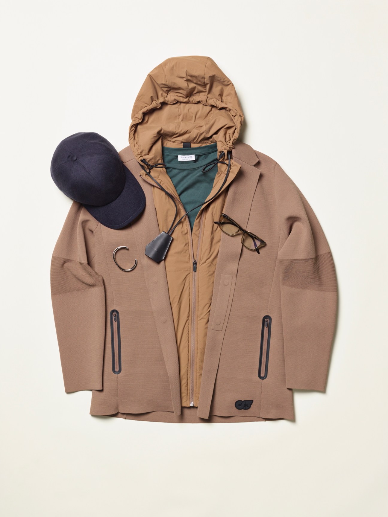 Layered autumn outerwear arrangement with brown jacket, tan puffer vest, navy cap and glasses on white background