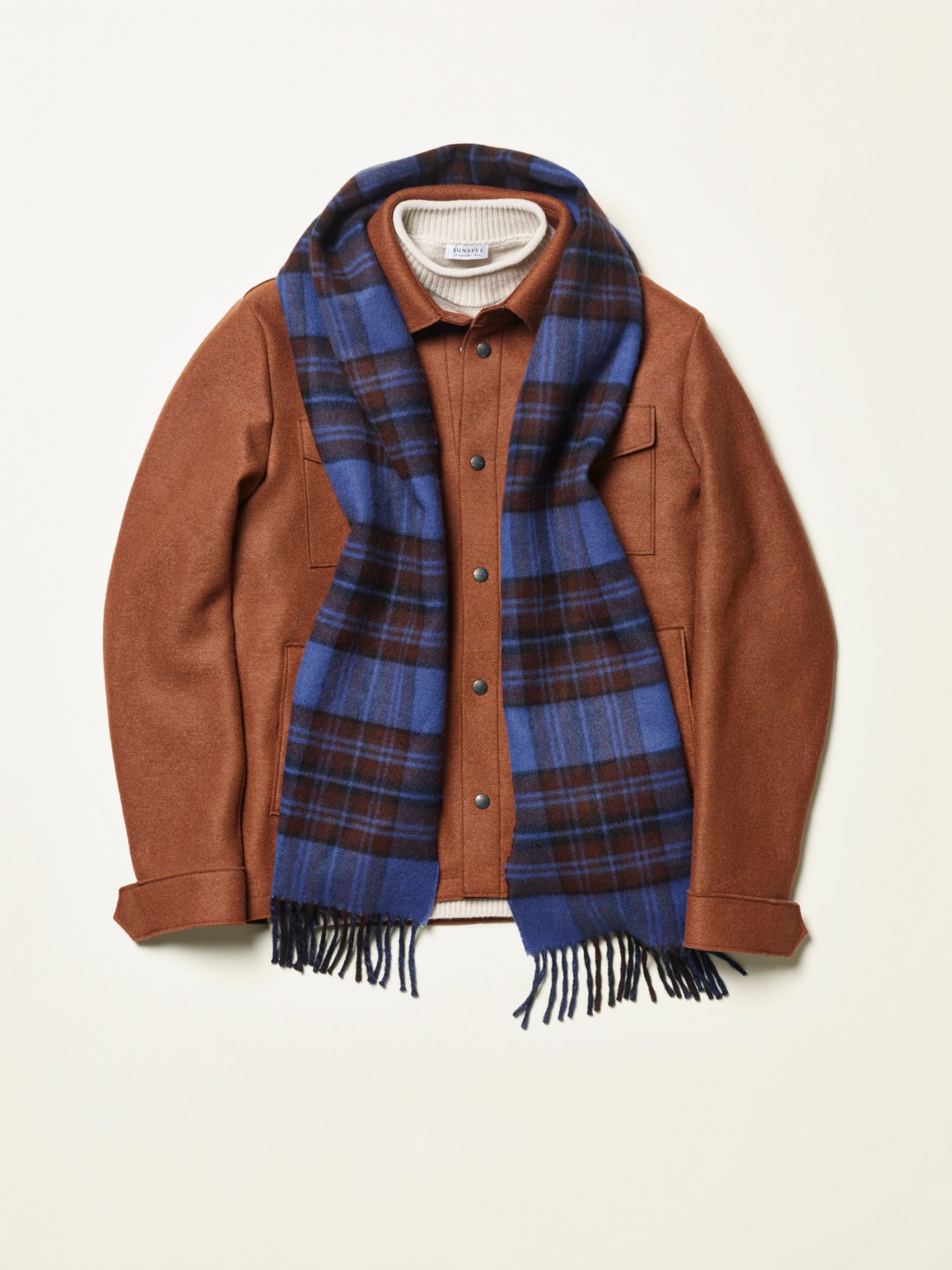 Brown wool jacket with blue tartan scarf and cream turtleneck sweater arranged as outfit on white background