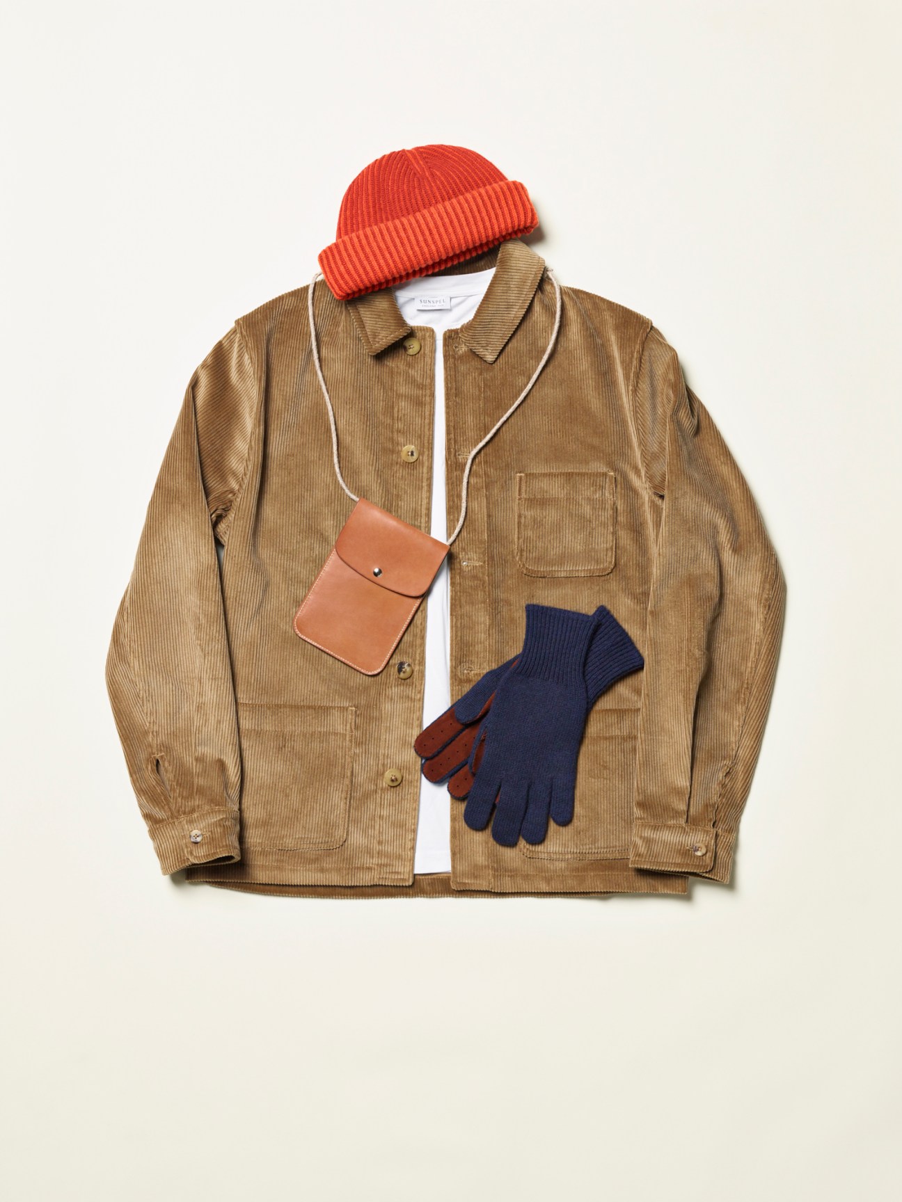 Brown corduroy jacket with orange knit beanie, navy gloves, and tan leather crossbody bag arranged on white background
