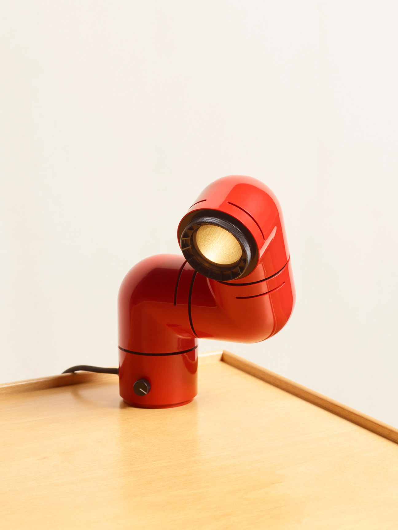 Red adjustable Tatu lamp with three rotating sections positioned on wooden surface