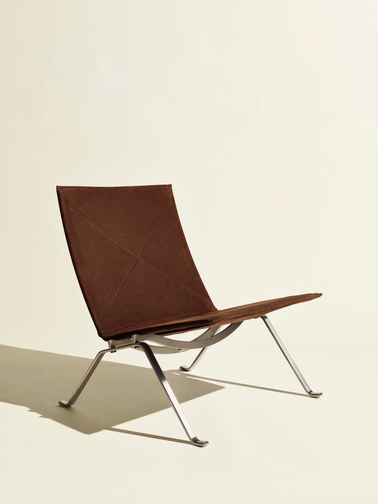 PK22 chair with brown leather seat and steel frame against cream background