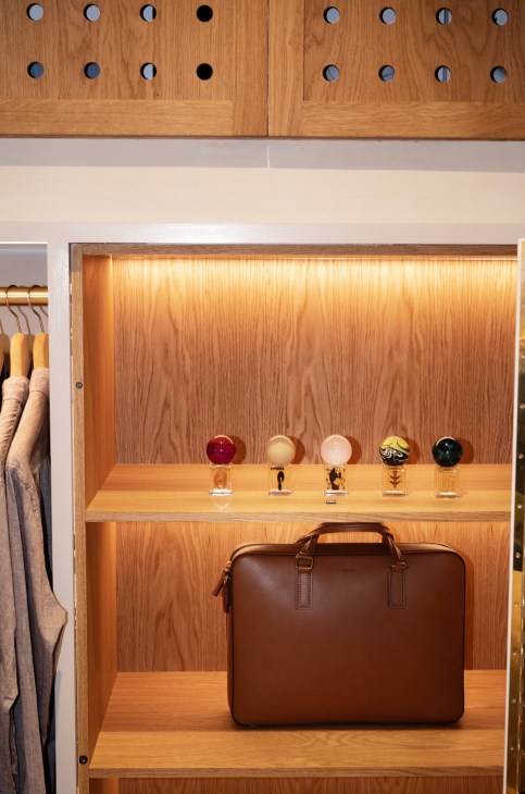 Brown leather bag and colorful fragrance bottles displayed on wooden shelf in menswear store