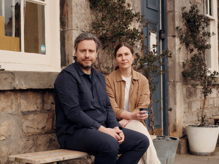 Kestin and Gemma Hare sitting together on a wooden bench outside a stone building
