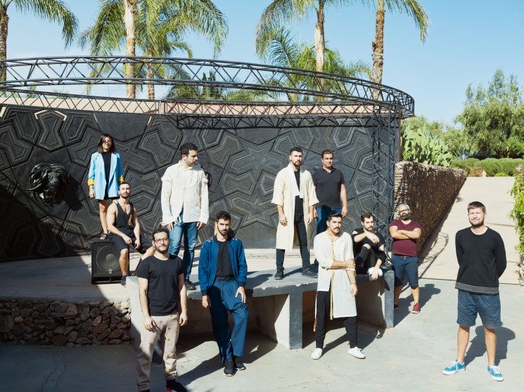 A group of people posing outdoors near a sculptural dark installation surrounded by palm trees.