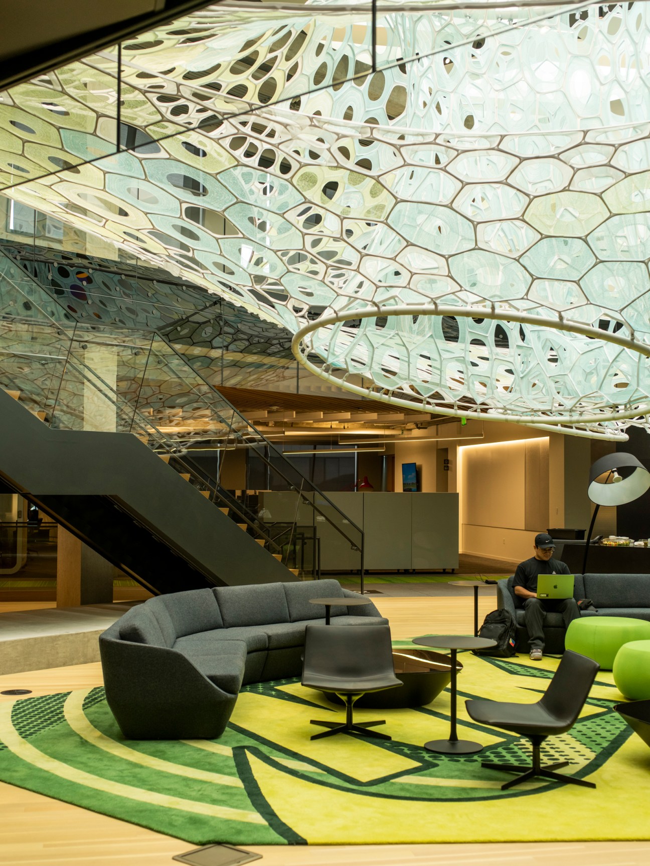 Modern interior space with perforated ceiling design, curved seating area, and person working on laptop