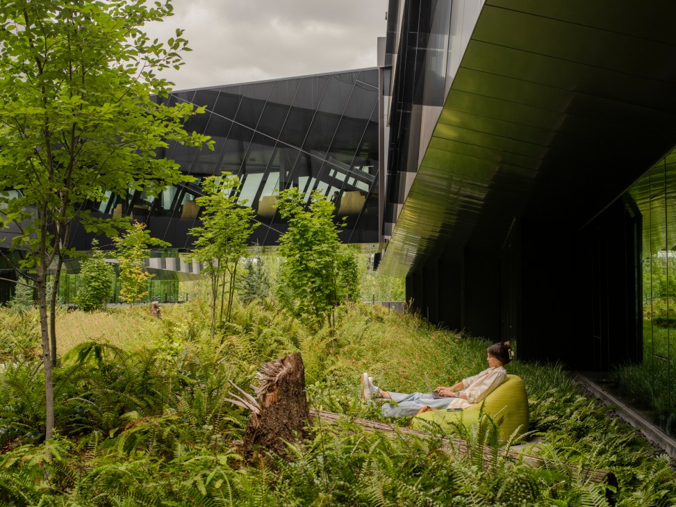 Person sitting in green chair reading in landscaped garden area with modern architecture and lush vegetation