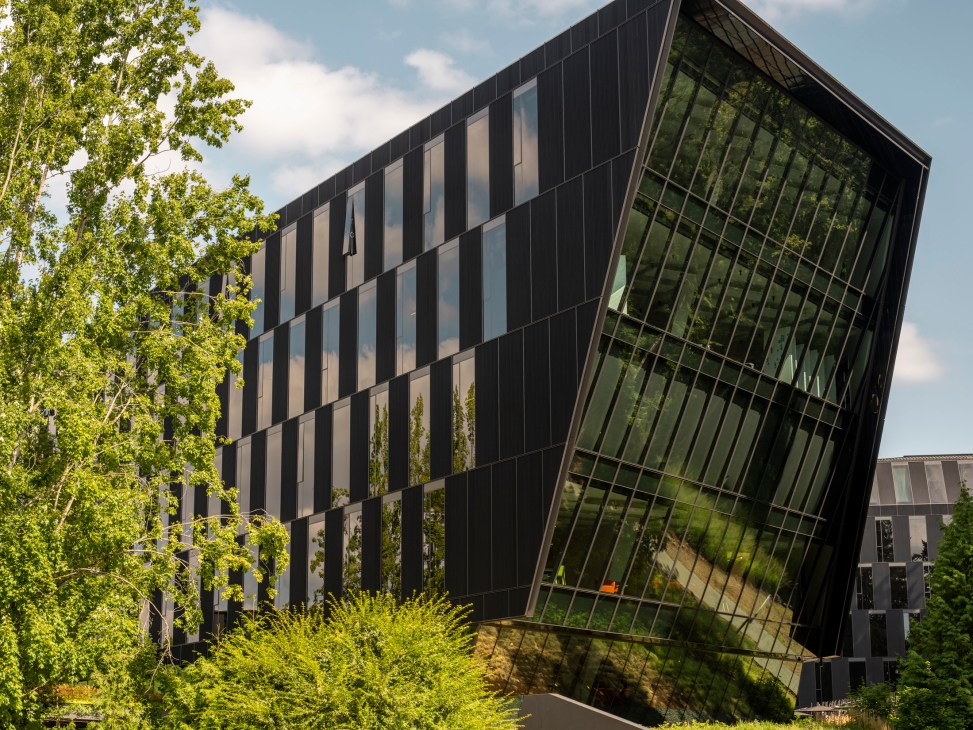 Modern angular building with dark exterior panels and large angled glass windows reflecting surrounding trees
