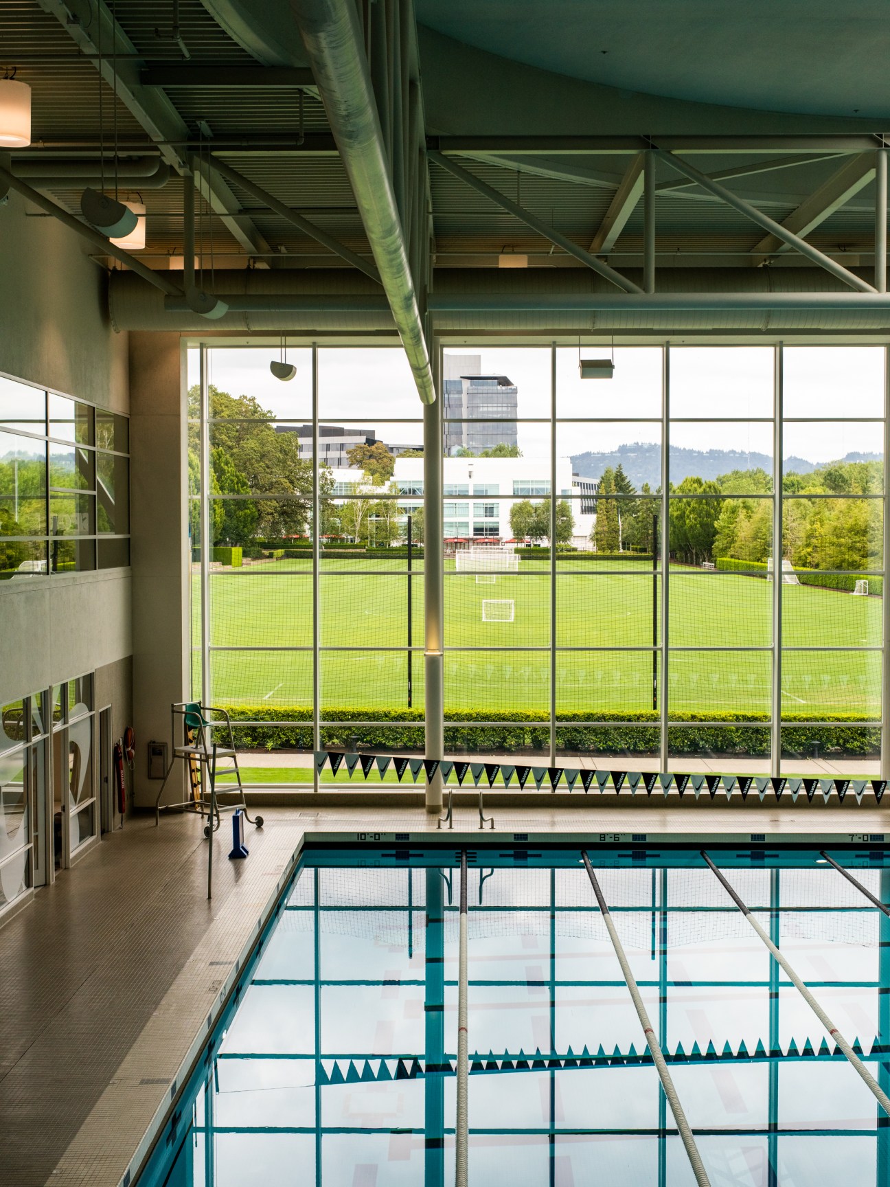 Indoor swimming pool with lane dividers overlooking outdoor sports fields through large windows