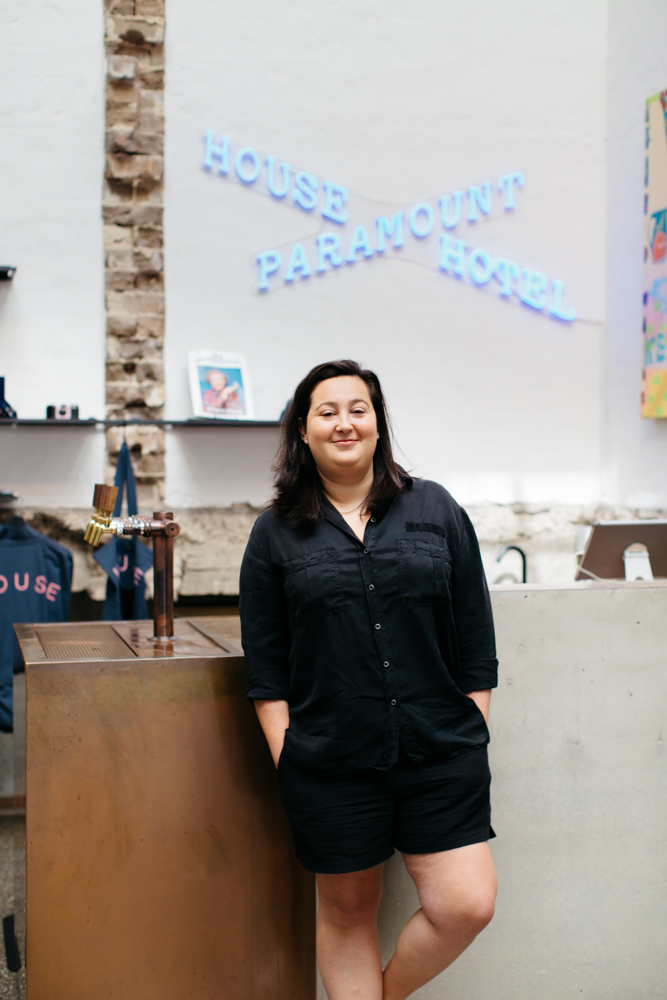 Eden Elan, general manager of Paramount House Hotel in Sydney, stands in the hotel lobby beneath a blue neon sign.