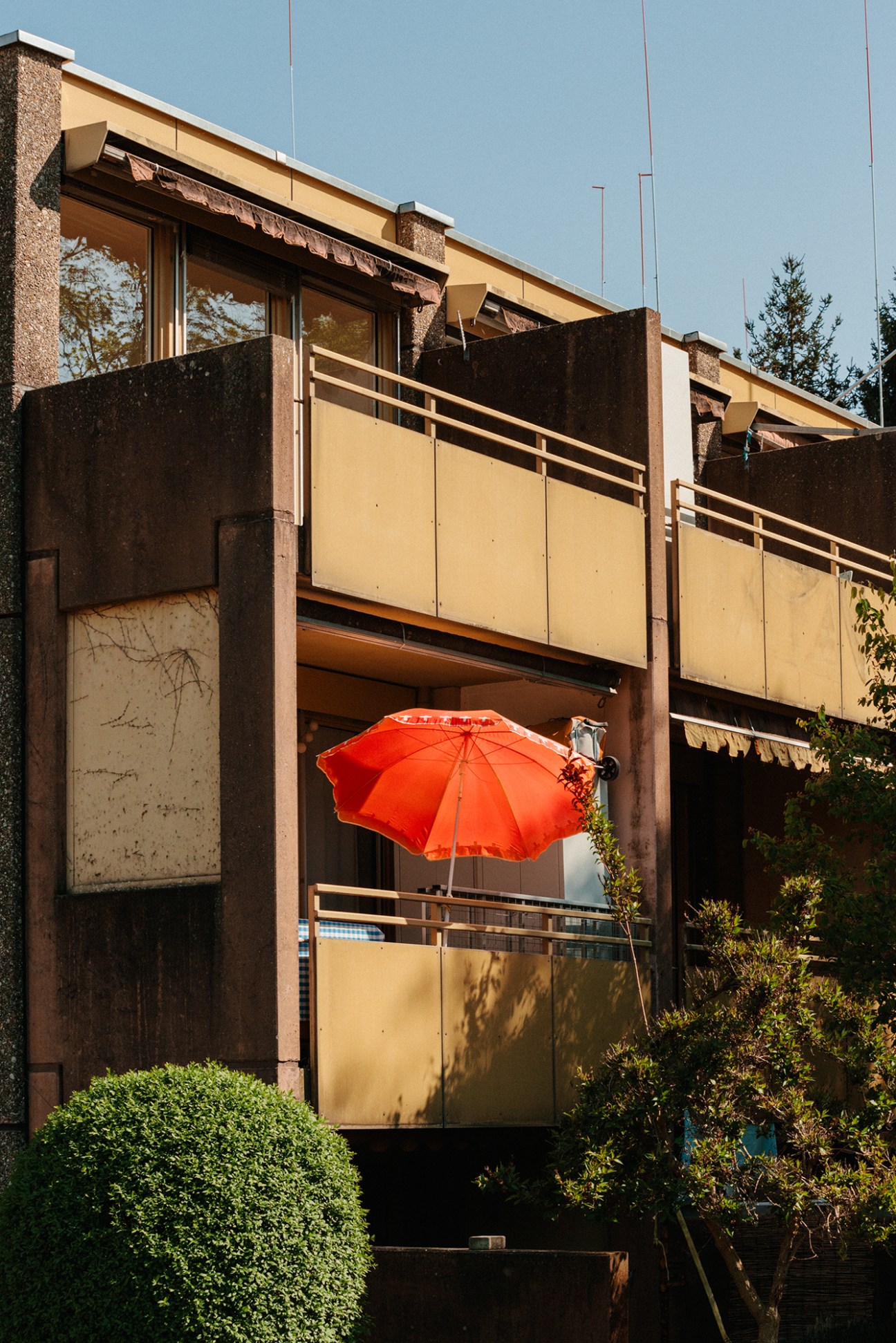 Residential balcony with orange umbrella, wooden railings and greenery creating shaded outdoor living space
