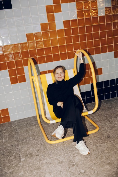 Barbara Elwardt sitting on yellow exercise equipment against colorful mosaic tile wall