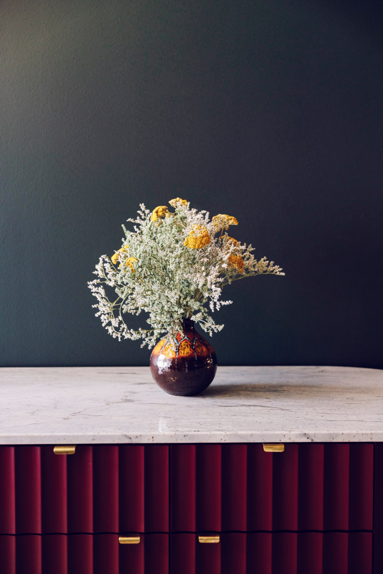 Fresh flower bouquet arranged in dark ceramic vase on marble counter surface against dark wall