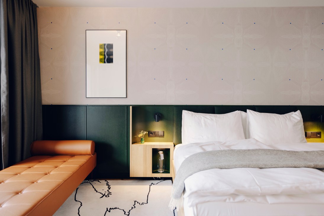 Hotel room with white bedding, orange leather bench, dark green headboard wall, and framed artwork