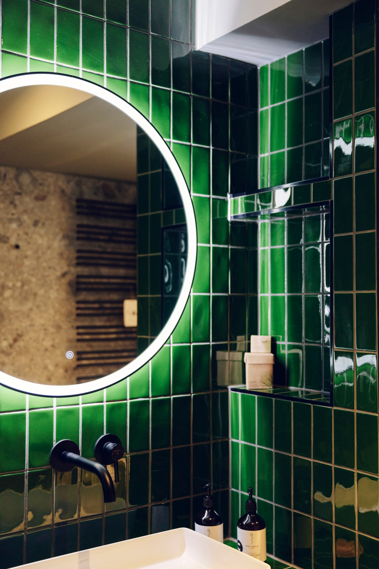 Modern bathroom with bottle-green tiles, round mirror, and contemporary fixtures