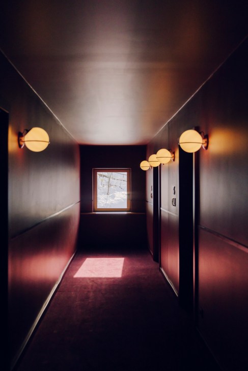 Modern hotel corridor with warm lighting, spherical pendant lamps, and wooden paneling leading to guest rooms