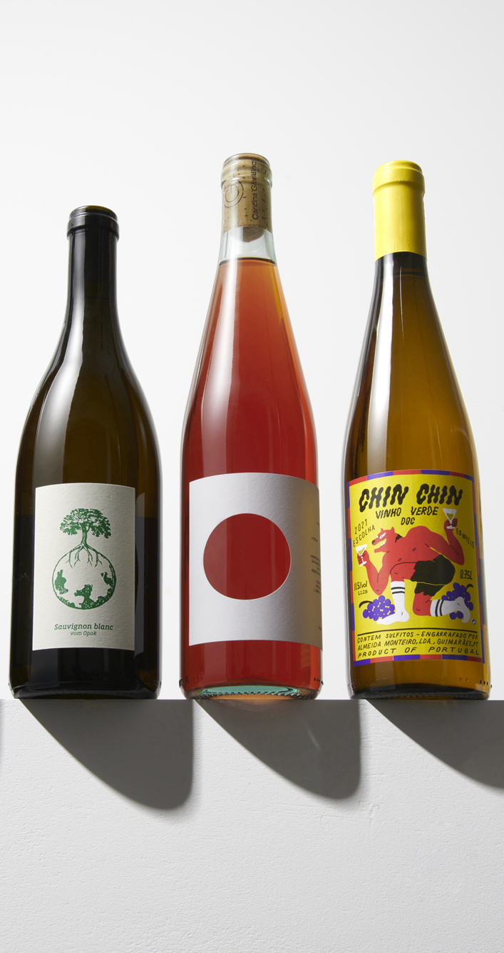 Three wine bottles with distinctive label designs - minimalist tree logo, simple red circle, and colorful cartoon graphics