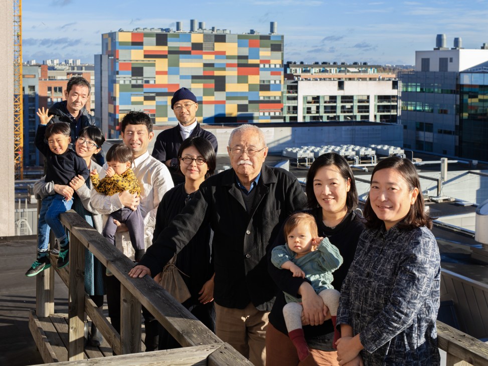 Group of Japanese residents posing together on a rooftop terrace with colorful Helsinki buildings in the background